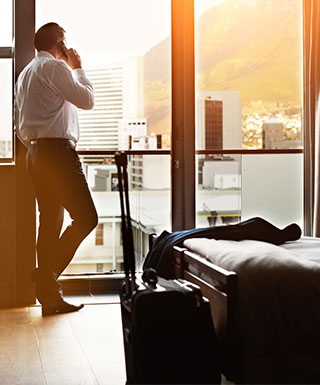 man talking on a cell phone leaning on a window in a hotel room