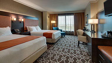 brown pattern carpet, two queen sized bed with orange blanket, teal chair, window curtain open
