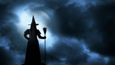 Witch with a broom standing in the dark clouds